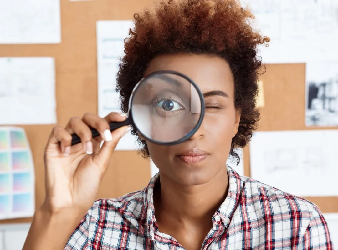 Young beautiful african worker holding magnifier infront of eye.